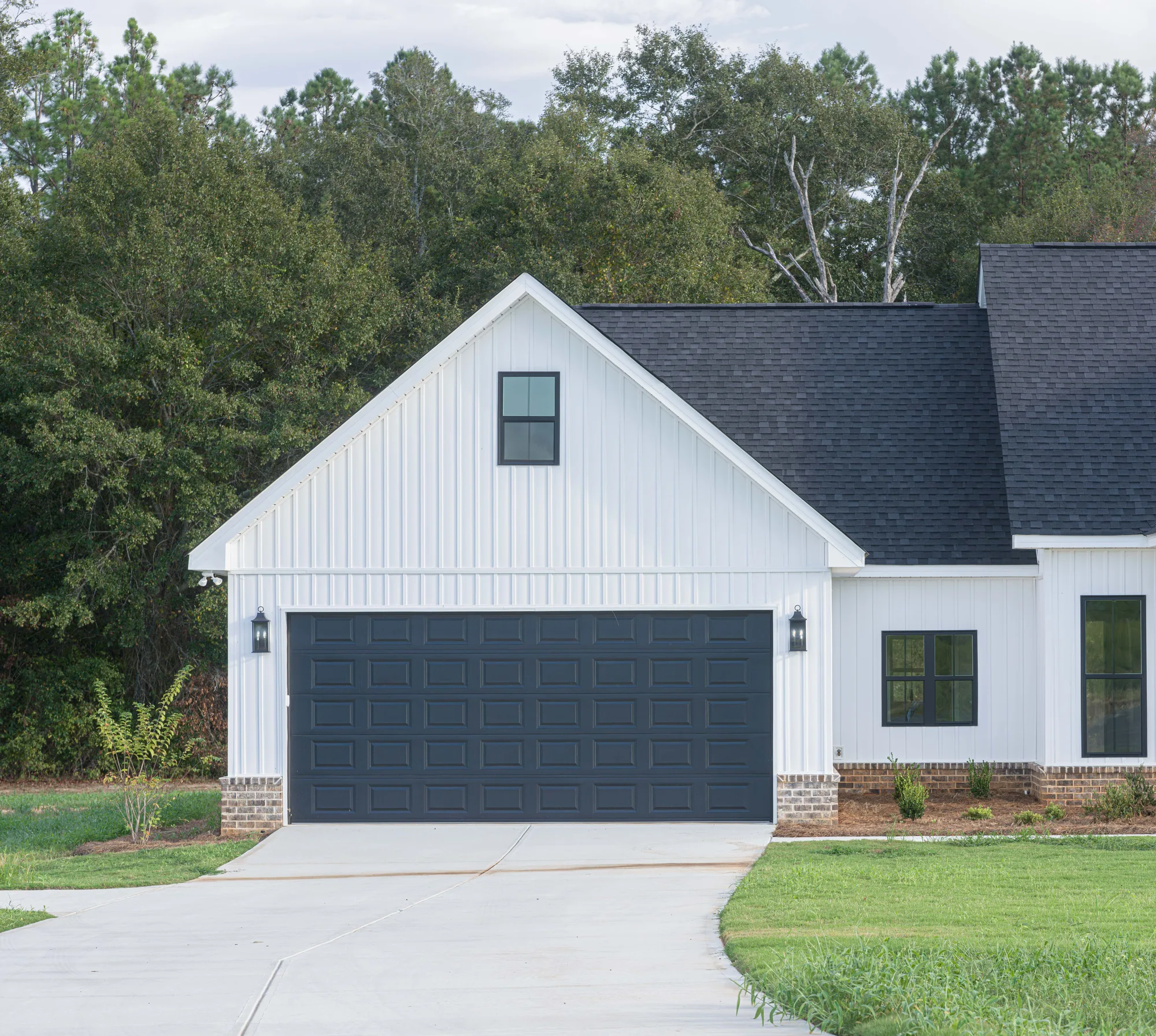 Charcoal raised-panel double garage door on a white board-and-batten farmhouse with a curved concrete drive