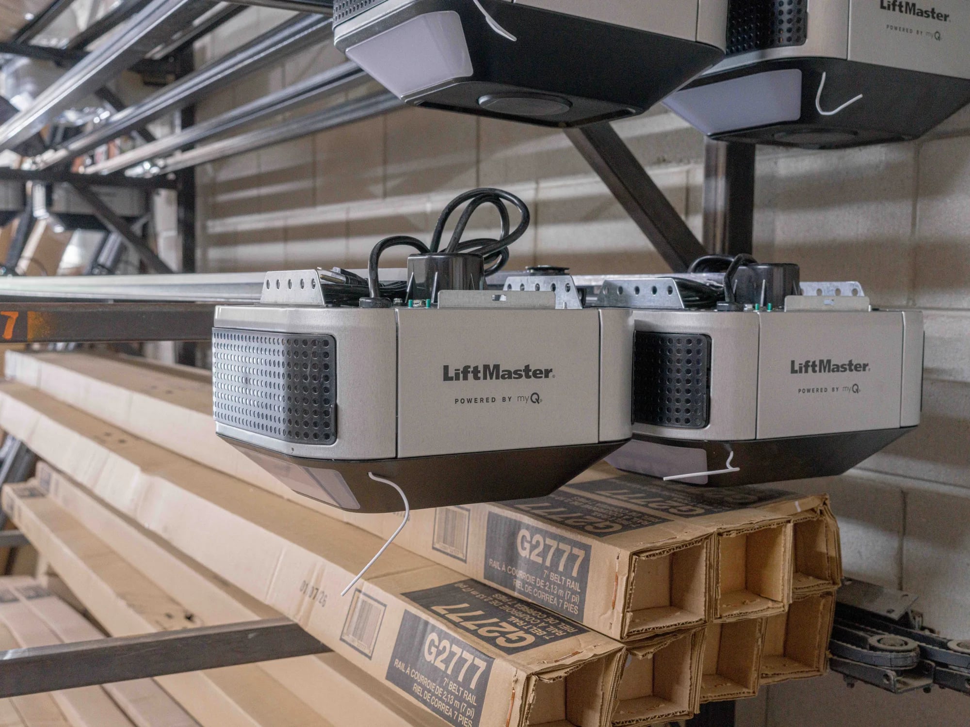 Two LiftMaster garage door openers on a shop rack above boxed belt rails