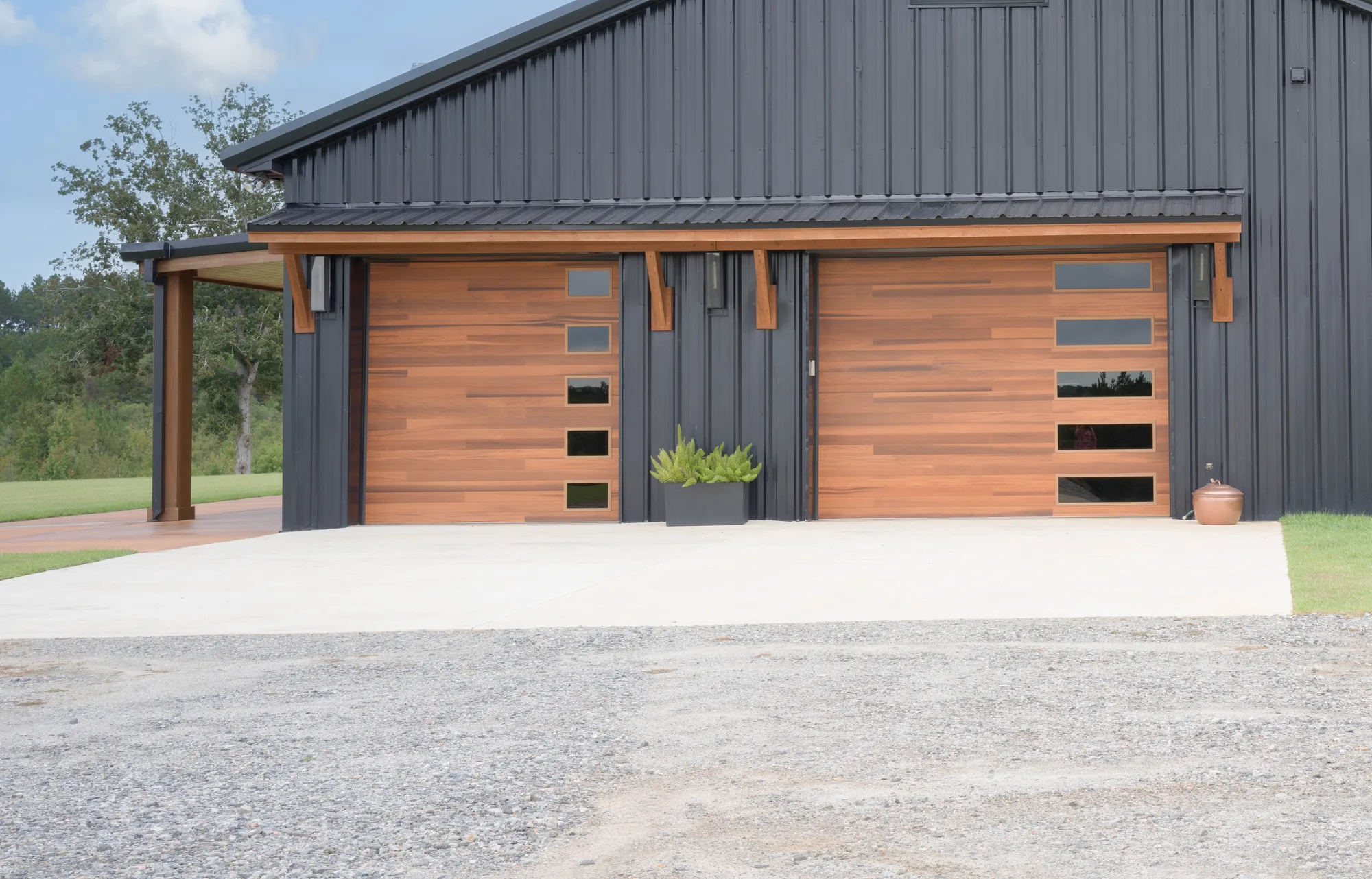 Two cedar-tone plank garage doors with stacked side windows on a black metal building