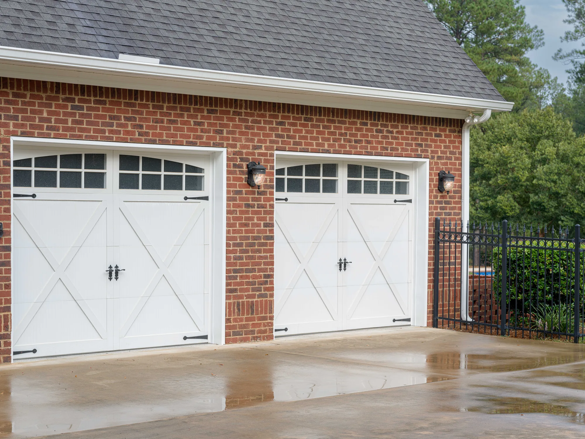 White crossbuck carriage-style garage doors with arched top windows on a red brick garage