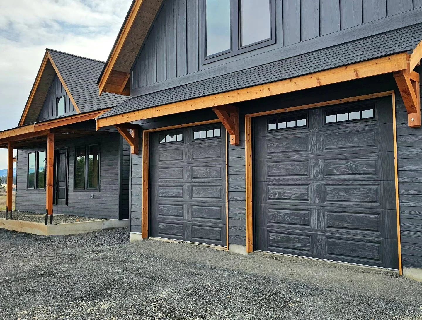 CHI raised-panel garage doors in a carbon oak woodgrain finish on a charcoal board-and-batten home with cedar beams