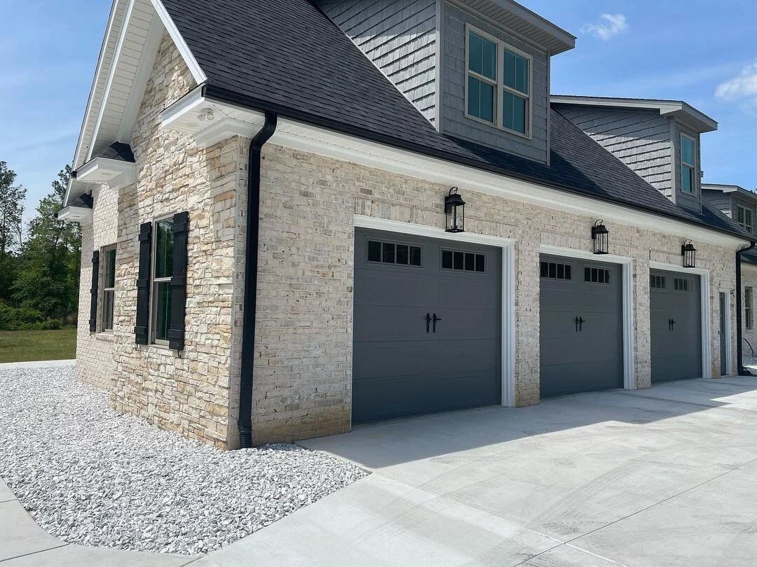 Three graphite carriage-style garage doors with decorative hardware on a stone and shake-sided home