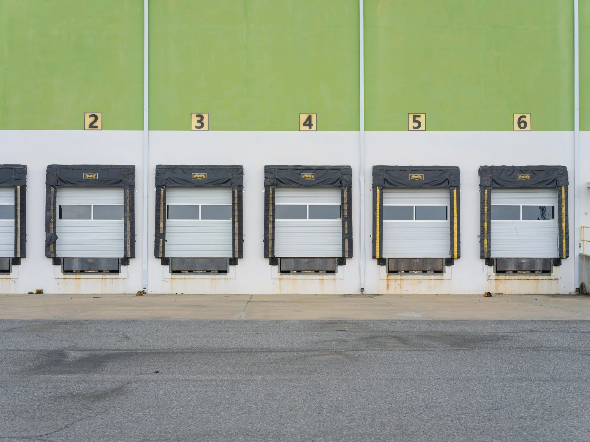 Five numbered loading dock positions on a green and white warehouse wall, each with a white sectional door, a black dock seal and a leveler