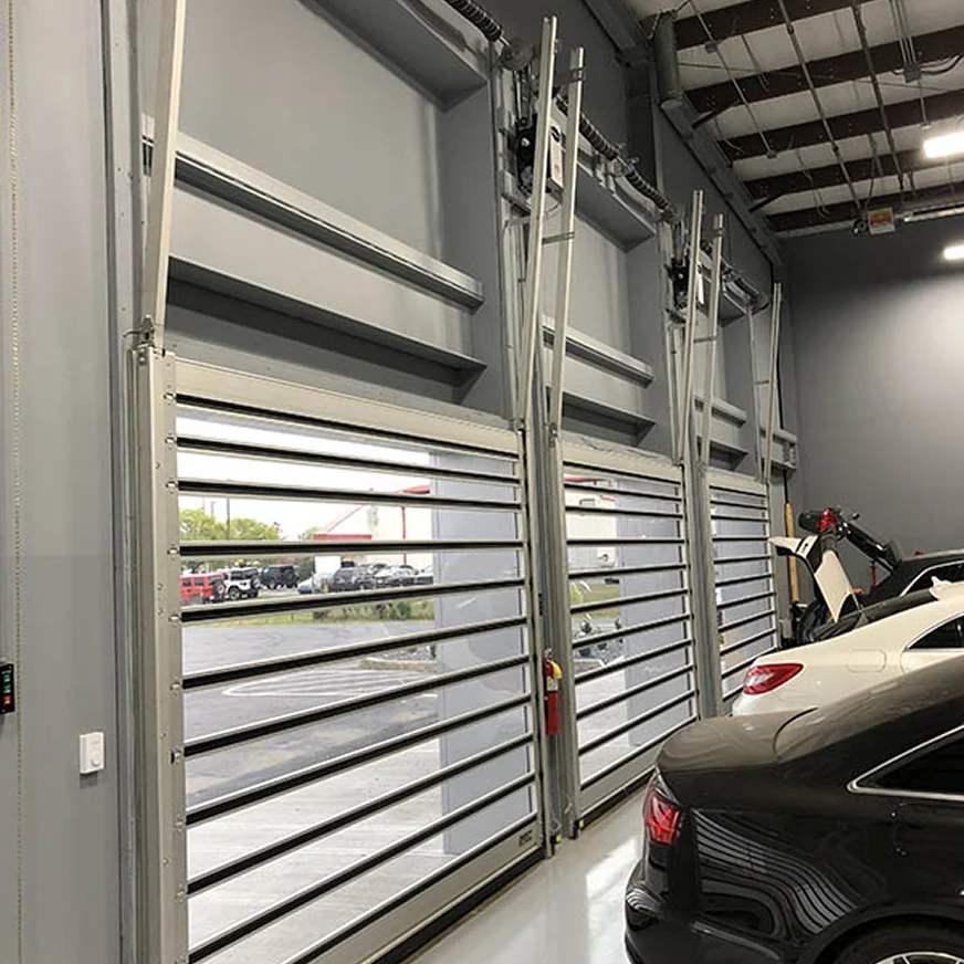Three high-speed rigid rolling doors with vision slats seen from inside a service bay, cars parked beside them
