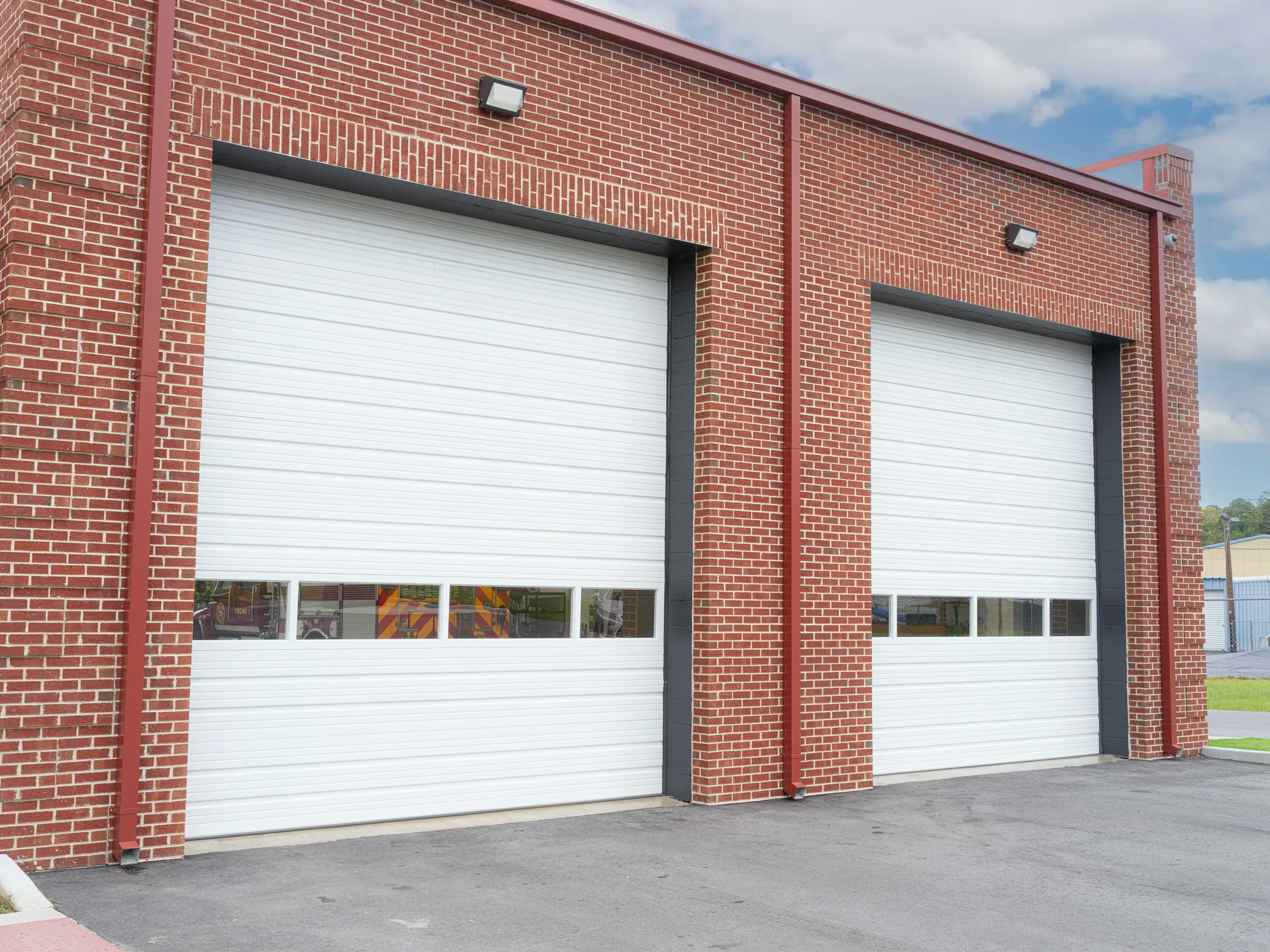 Two tall white insulated sectional steel doors with a row of vision panels in a red brick wall