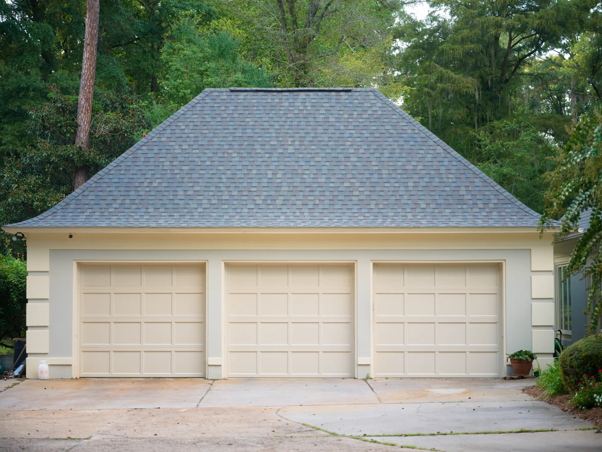 Three cream recessed-panel garage doors on a cream stucco garage with a hip roof
