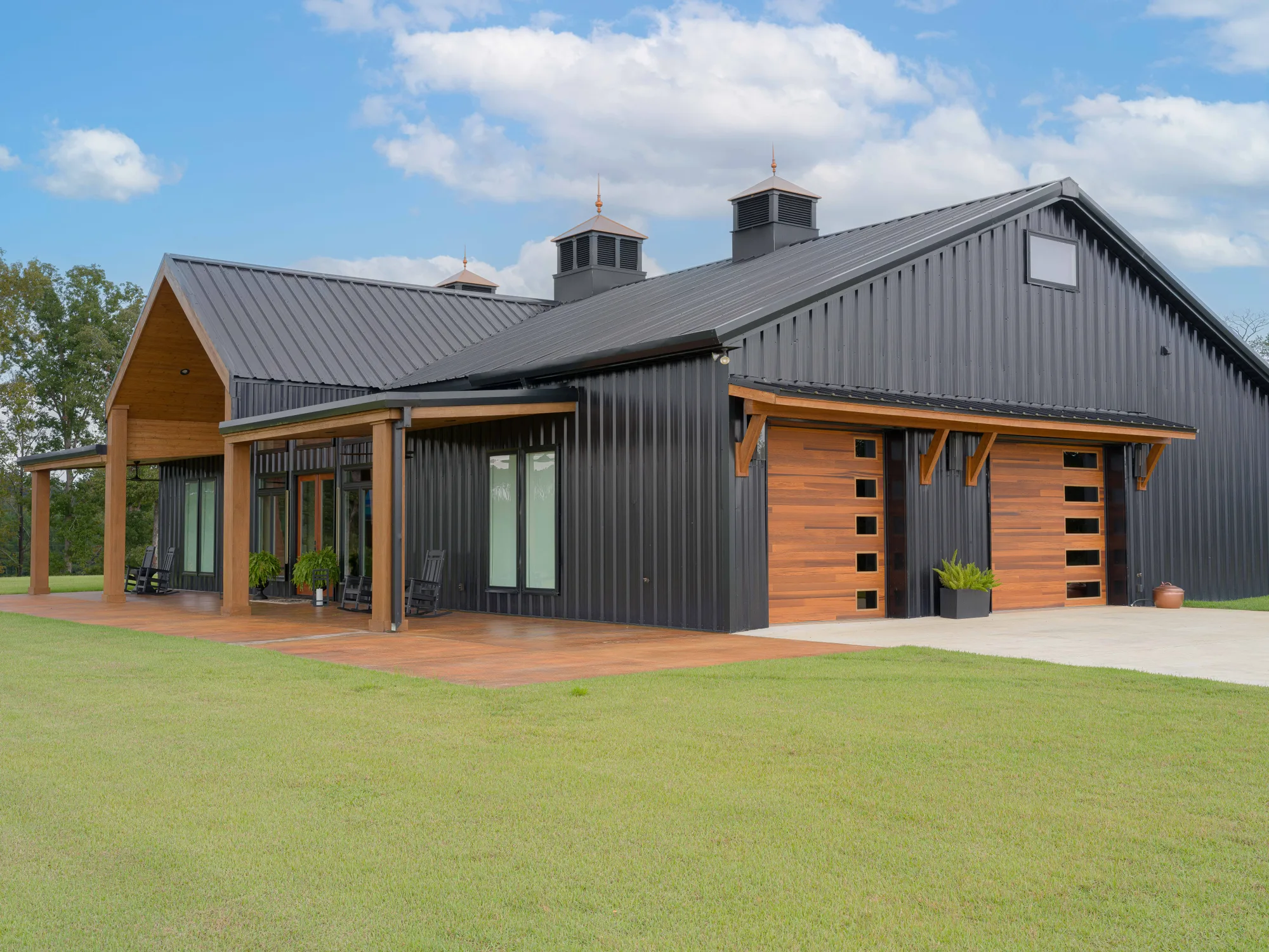 Black metal home with a timber porch and two cedar-tone plank garage doors with stacked side windows