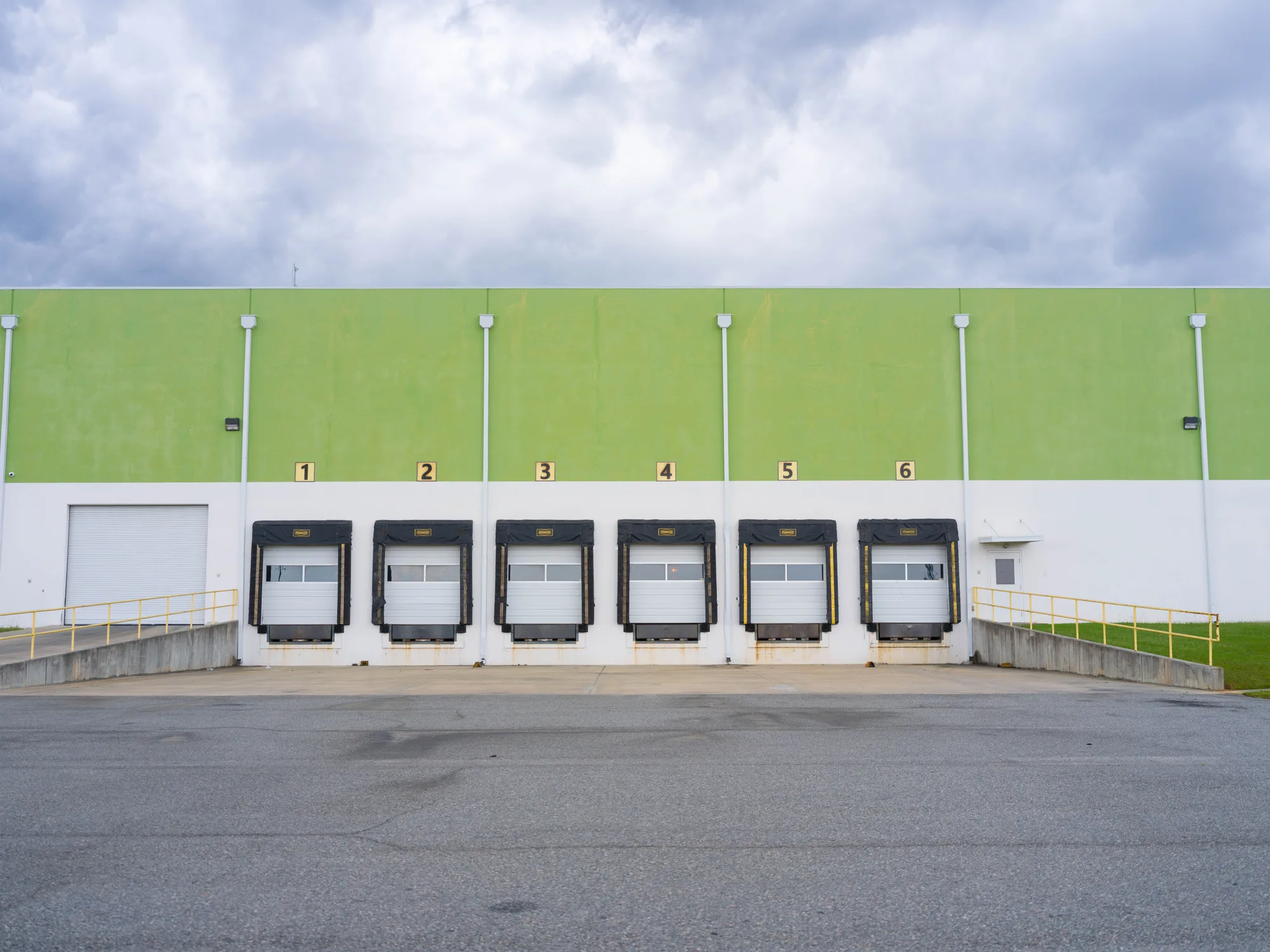 Six numbered loading dock doors with black dock seals on a green and white warehouse wall