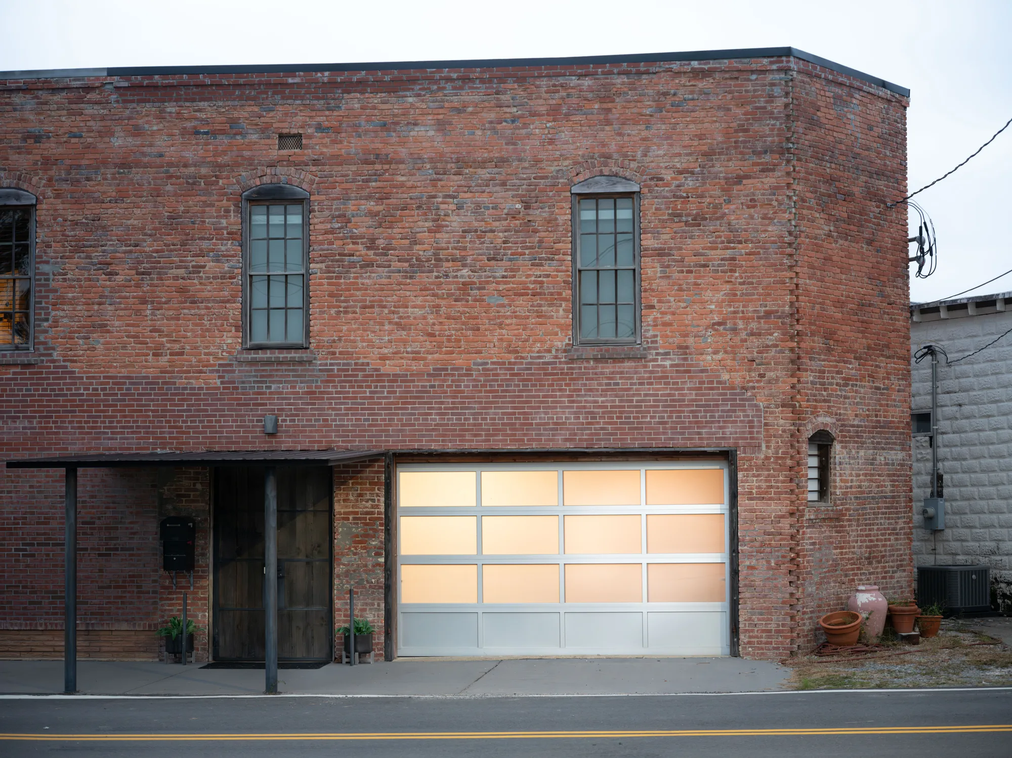 Frosted full-view glass garage door in an aluminum frame, lit from inside, on a two-story red brick building