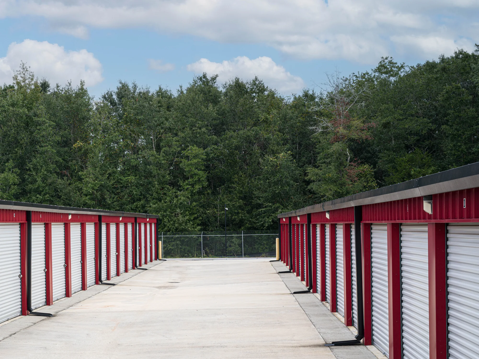 Rows of white roll-up doors in red steel frames on both sides of a concrete drive aisle at a self-storage facility