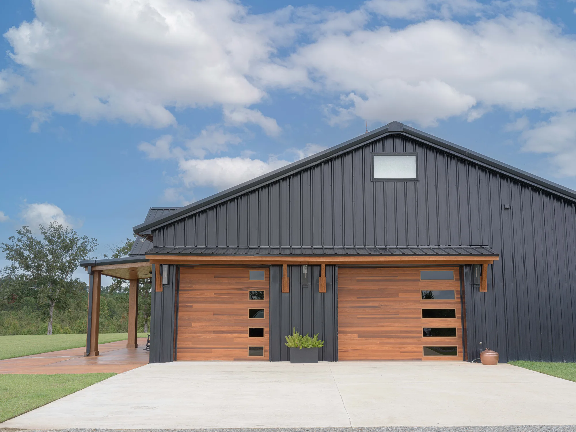 Two cedar-tone plank garage doors with stacked side windows under a timber awning on a black metal building