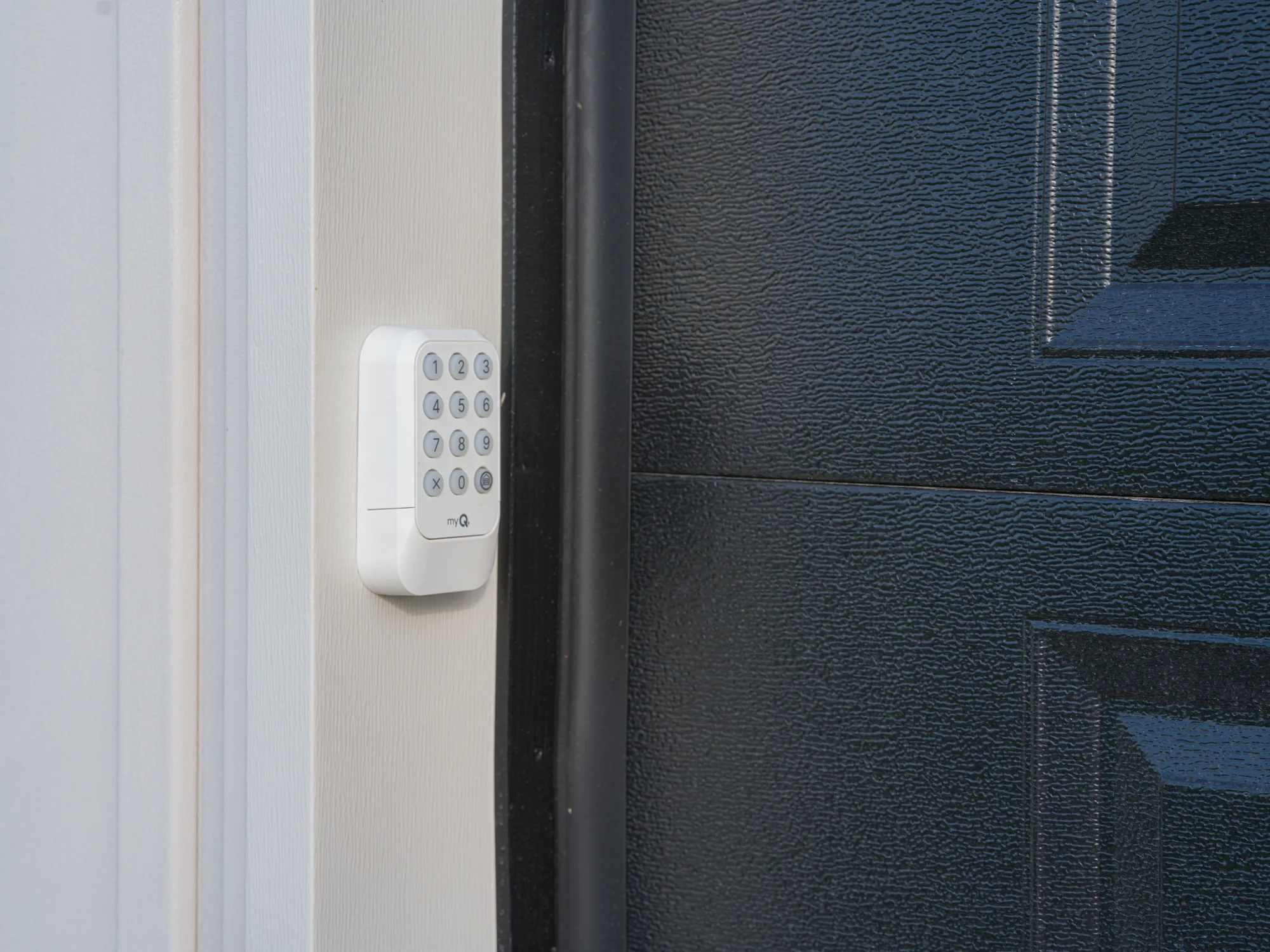 White wireless keypad mounted on the white frame beside a charcoal raised-panel garage door