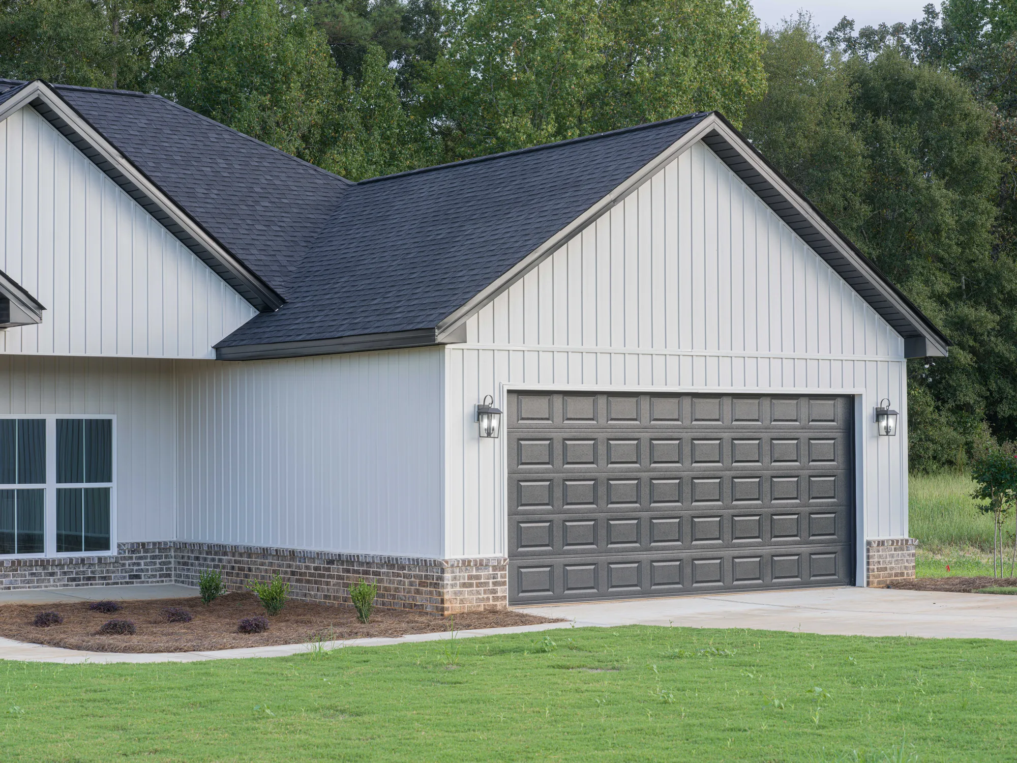 Charcoal raised-panel double garage door on an off-white board-and-batten home